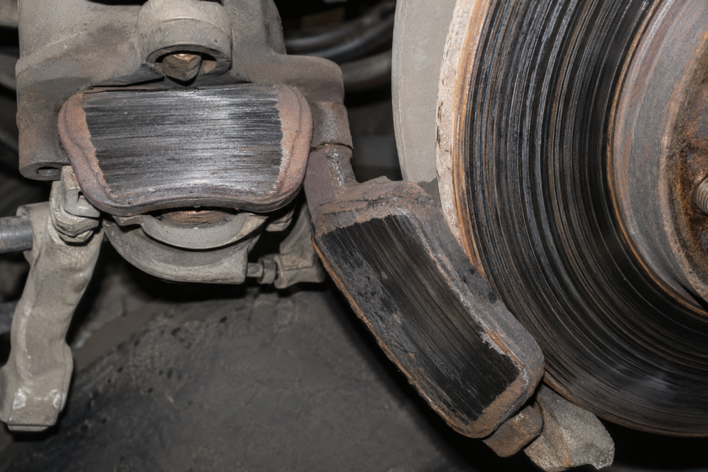 Severely worn heavy-truck brake pads beside a deeply grooved rotor, showing uneven wear and possible brake system faults
